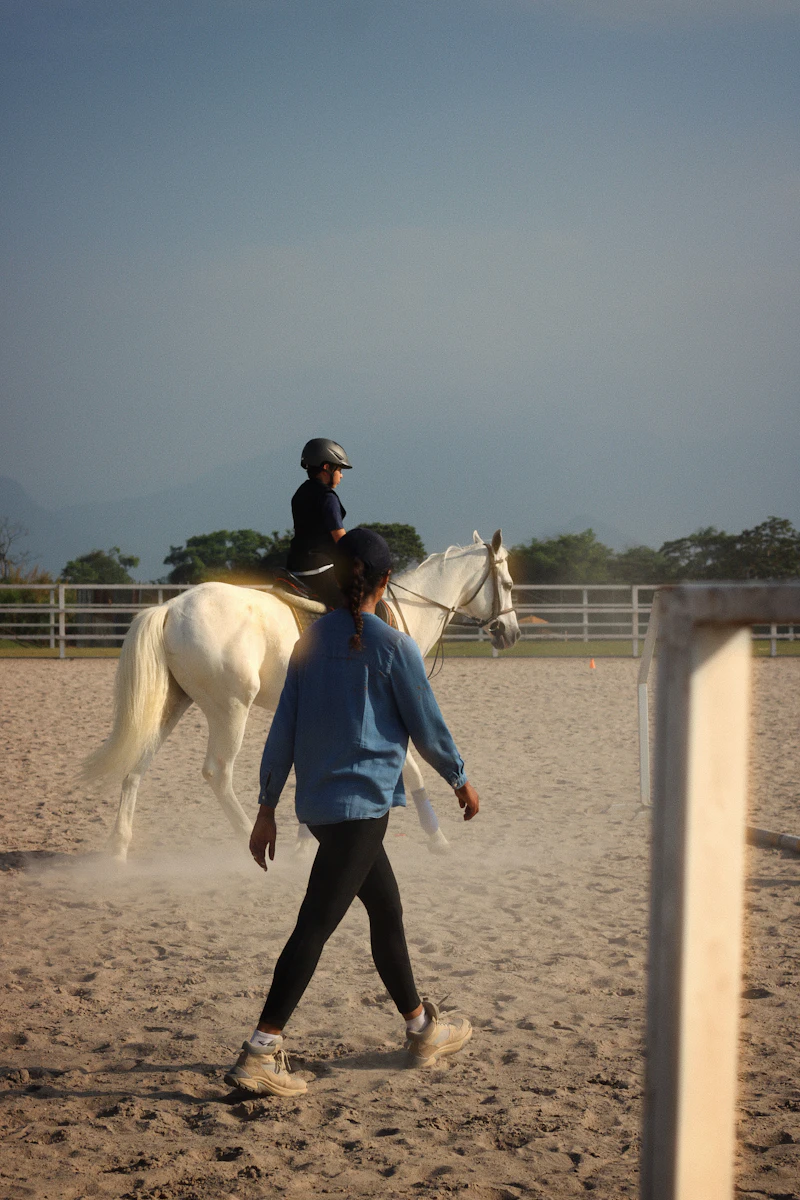 An instructor leading a beginner on a grey horse in the arena
